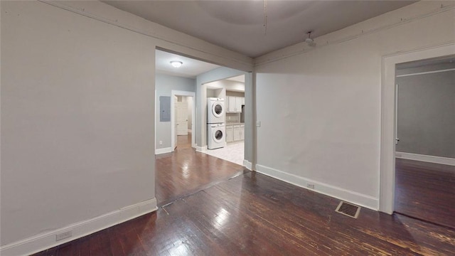 empty room with stacked washing machine and dryer, baseboards, wood-type flooring, and electric panel