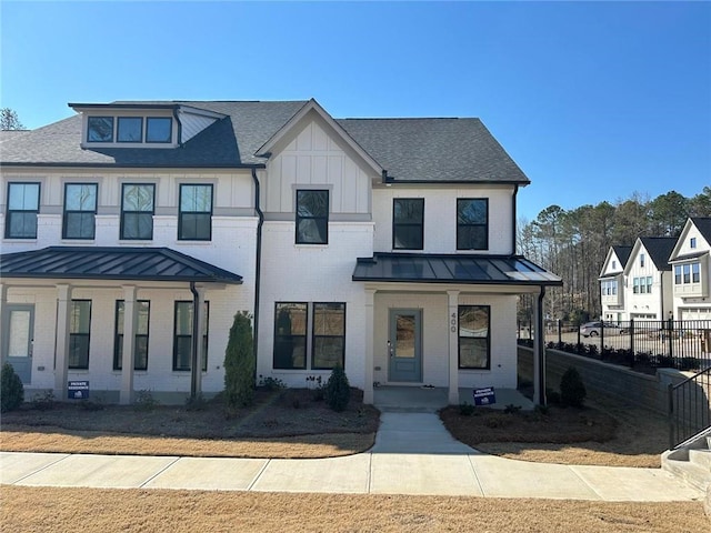 view of front of house featuring brick siding, covered porch, board and batten siding, a standing seam roof, and fence