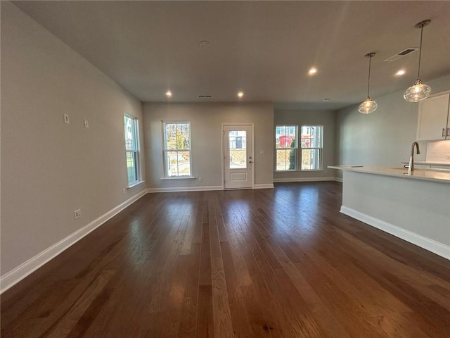 unfurnished living room featuring dark wood-type flooring, a wealth of natural light, visible vents, and a sink