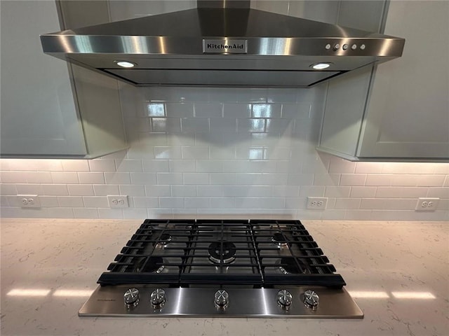 details featuring stainless steel gas stovetop, light stone counters, ventilation hood, and backsplash