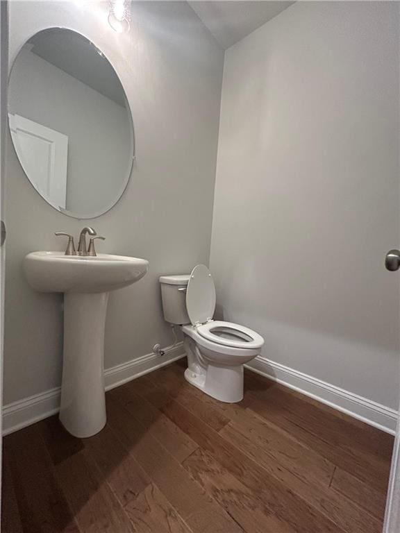 half bath with toilet, baseboards, and wood finished floors