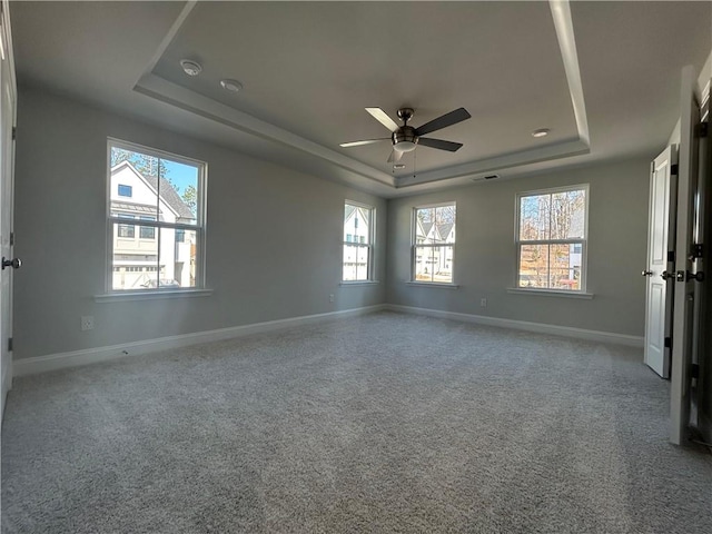 unfurnished bedroom featuring a ceiling fan, baseboards, a tray ceiling, and carpet flooring