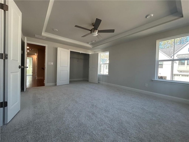 unfurnished bedroom featuring a tray ceiling, a closet, light colored carpet, and baseboards