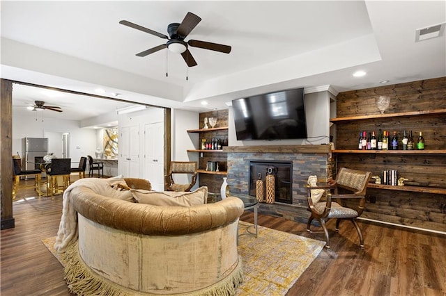 living room with dark hardwood / wood-style flooring, a tray ceiling, a stone fireplace, and ceiling fan