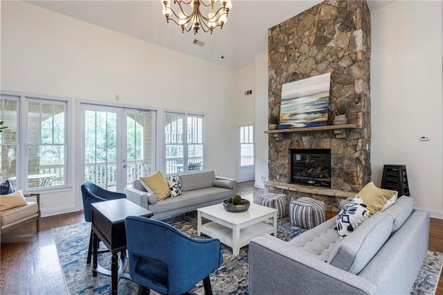 living room with dark hardwood / wood-style floors, a stone fireplace, a towering ceiling, and a chandelier