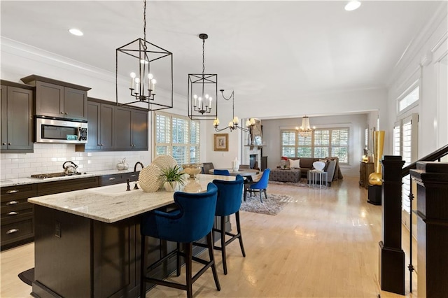 kitchen featuring a breakfast bar, appliances with stainless steel finishes, a kitchen island with sink, hanging light fixtures, and dark brown cabinetry