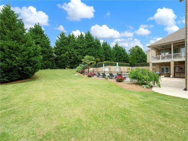 view of yard featuring a ceiling fan, a patio area, fence, and a balcony