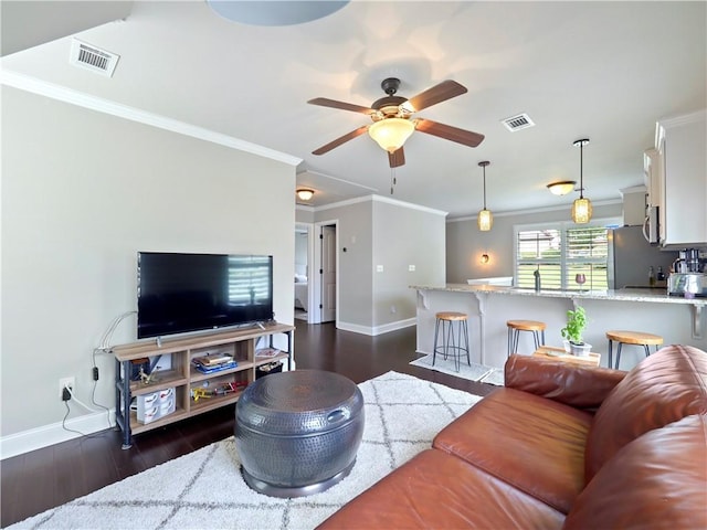 living area featuring visible vents, baseboards, crown molding, and dark wood-style floors