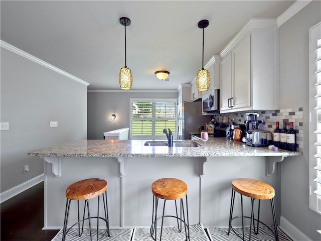 kitchen featuring white cabinets, appliances with stainless steel finishes, a sink, a peninsula, and baseboards