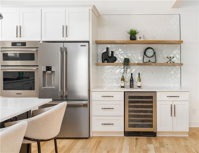 bar with decorative backsplash, beverage cooler, light wood-style floors, a dry bar, and stainless steel appliances