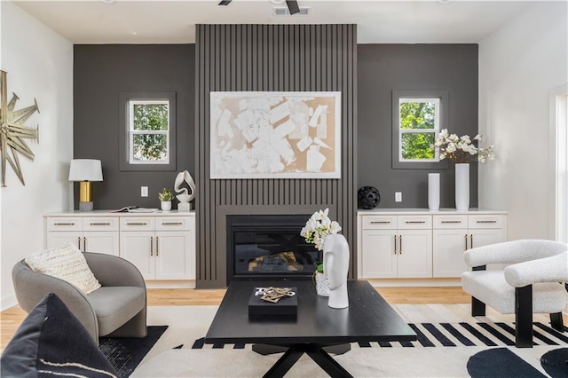 living room featuring a glass covered fireplace, visible vents, and light wood-style flooring