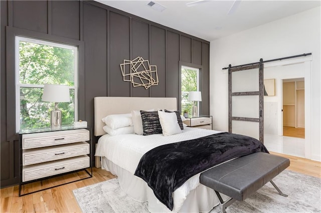 bedroom with a ceiling fan, visible vents, light wood-style floors, and a barn door
