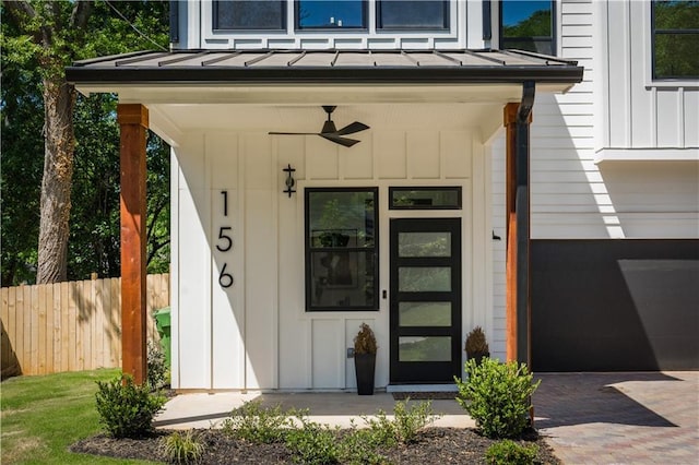 view of exterior entry with a garage, board and batten siding, fence, metal roof, and a standing seam roof
