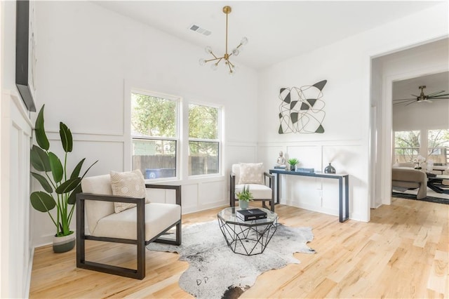 sitting room featuring a wainscoted wall, visible vents, light wood-style floors, a chandelier, and a decorative wall