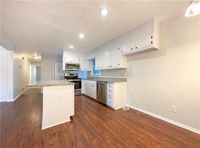 kitchen with a kitchen island, appliances with stainless steel finishes, dark hardwood / wood-style floors, white cabinetry, and light stone countertops