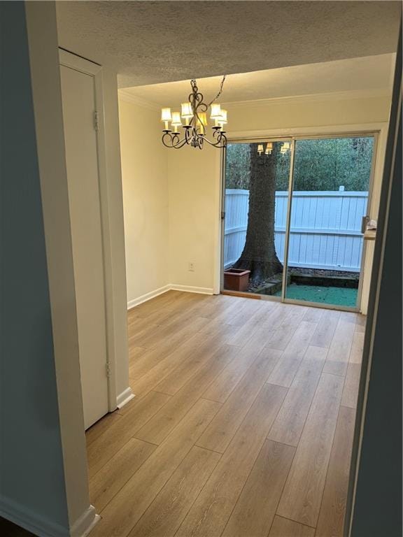 unfurnished dining area with a notable chandelier, light wood-type flooring, and a textured ceiling