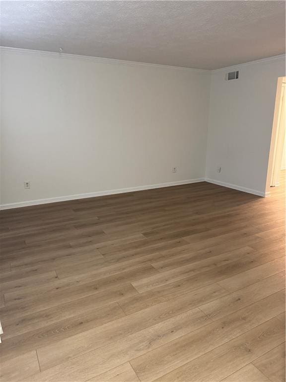 empty room with a textured ceiling, light wood-type flooring, and ornamental molding