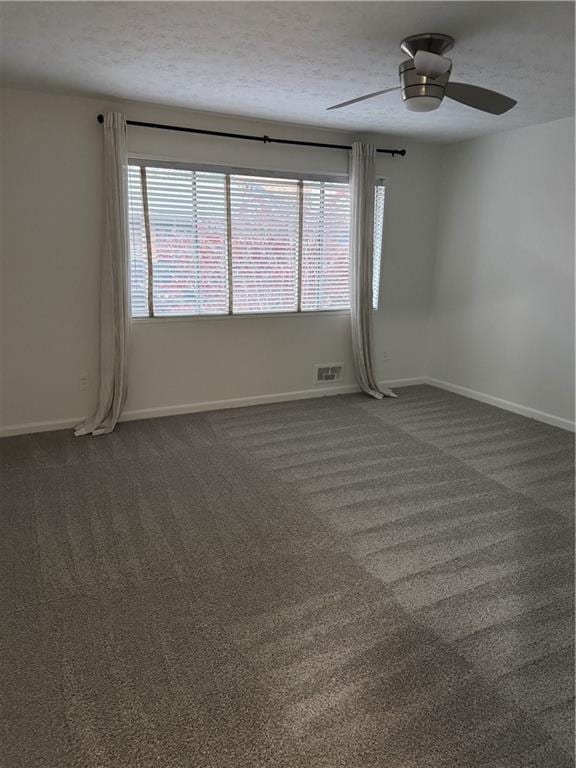 spare room featuring a textured ceiling, dark carpet, and ceiling fan