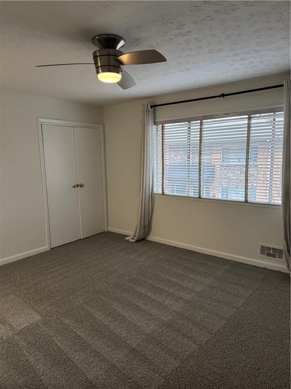 carpeted spare room featuring a textured ceiling, a wealth of natural light, and ceiling fan