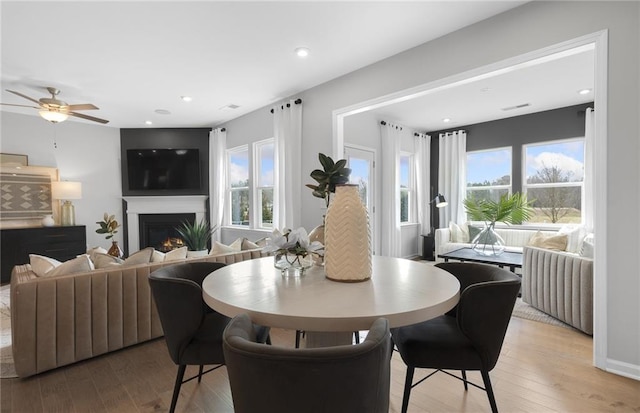 dining area with plenty of natural light, a lit fireplace, and light wood finished floors