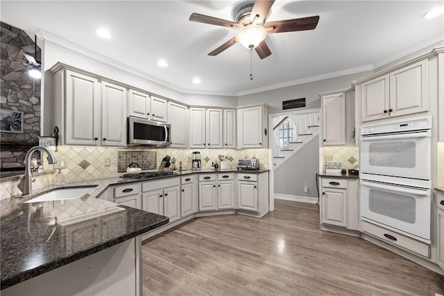 kitchen with dark stone counters, sink, ceiling fan, appliances with stainless steel finishes, and light hardwood / wood-style floors