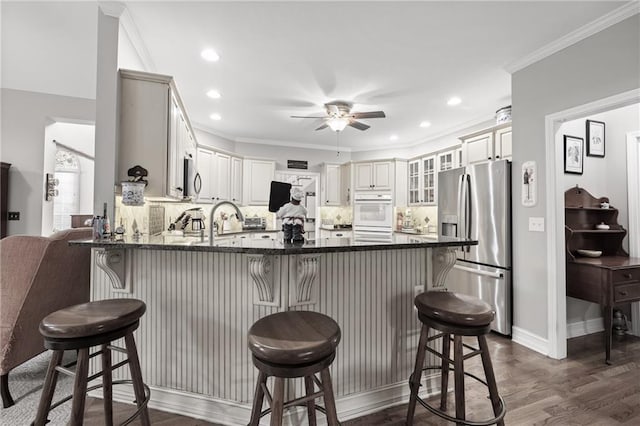 kitchen featuring ceiling fan, stainless steel refrigerator with ice dispenser, backsplash, kitchen peninsula, and a breakfast bar