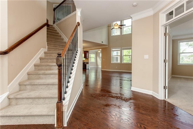 stairway with a healthy amount of sunlight, ceiling fan, crown molding, and wood finished floors