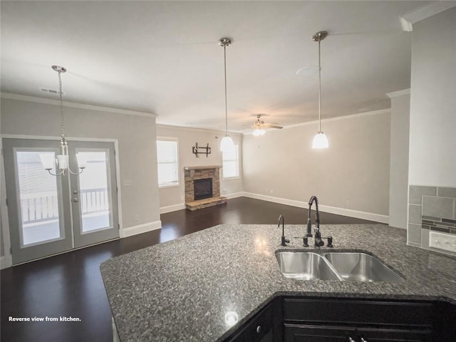 kitchen with ornamental molding, a stone fireplace, dark stone countertops, a ceiling fan, and a sink