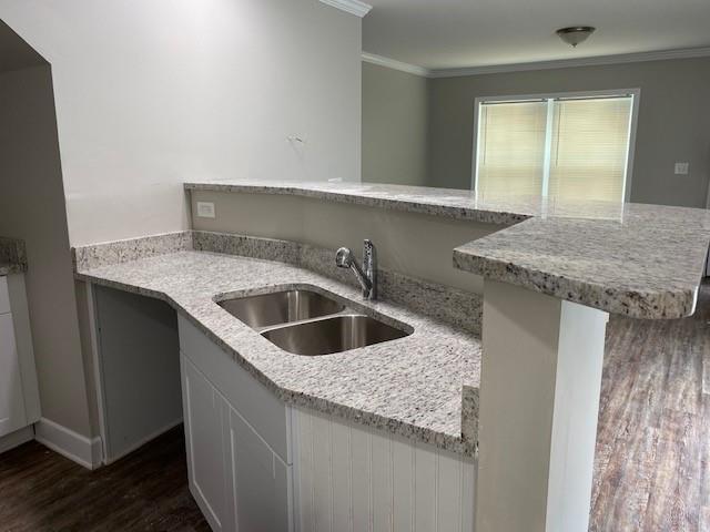 kitchen with a kitchen bar, dark hardwood / wood-style floors, ornamental molding, light stone counters, and sink