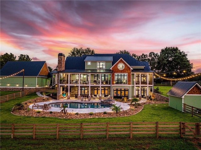 back house at dusk featuring a patio, a yard, a fenced in pool, a balcony, and a shed