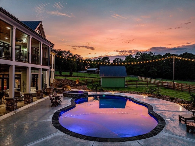 pool at dusk with a storage shed, an in ground hot tub, and a patio area