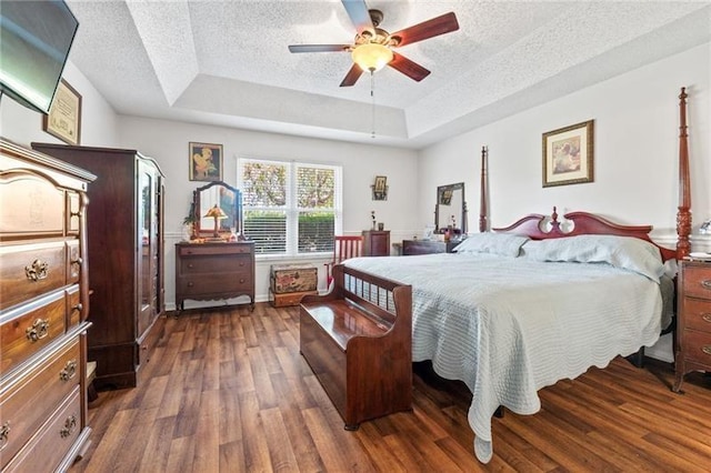 bedroom featuring a textured ceiling, a tray ceiling, ceiling fan, and dark wood-type flooring