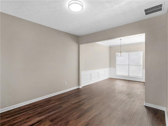 empty room featuring a textured ceiling, dark wood-type flooring, and an inviting chandelier