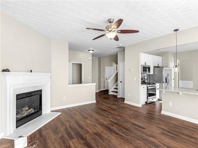 unfurnished living room featuring a fireplace, a textured ceiling, dark hardwood / wood-style floors, and ceiling fan