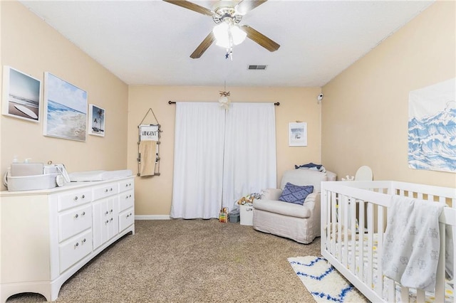 bedroom featuring a crib, a ceiling fan, visible vents, and light colored carpet