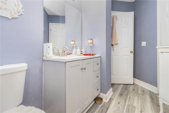 bathroom with vanity, toilet, wood finished floors, and baseboards