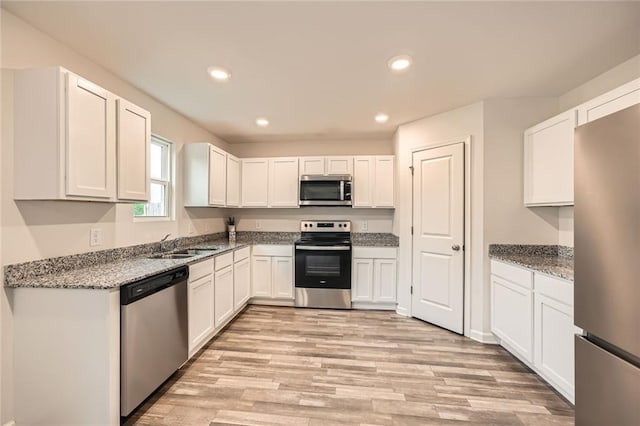 kitchen with white cabinets, appliances with stainless steel finishes, a sink, light wood-style flooring, and stone counters