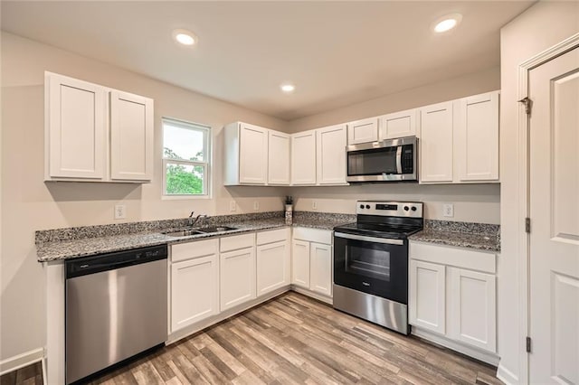 kitchen featuring light wood-type flooring, a sink, stone countertops, stainless steel appliances, and white cabinetry