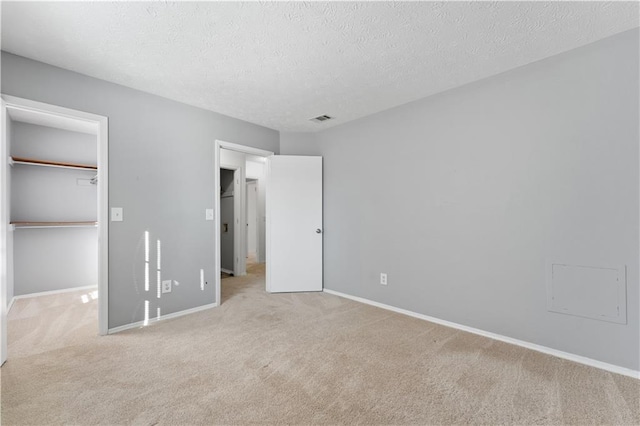 unfurnished bedroom featuring light carpet, a spacious closet, a closet, and a textured ceiling