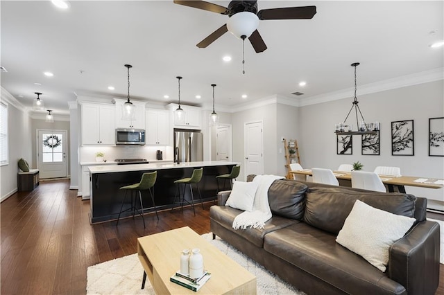 living room with dark wood-type flooring, crown molding, and ceiling fan with notable chandelier