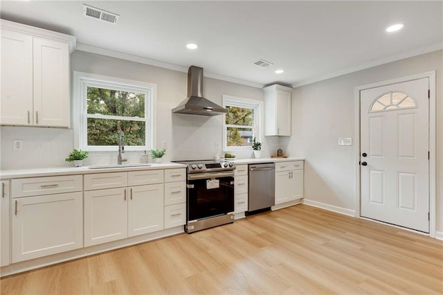 kitchen featuring wall chimney range hood, sink, light hardwood / wood-style flooring, appliances with stainless steel finishes, and white cabinetry