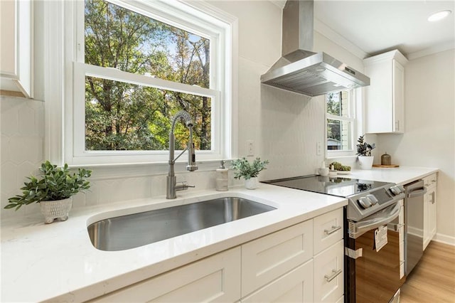 kitchen with sink, stainless steel appliances, wall chimney range hood, light hardwood / wood-style floors, and white cabinets