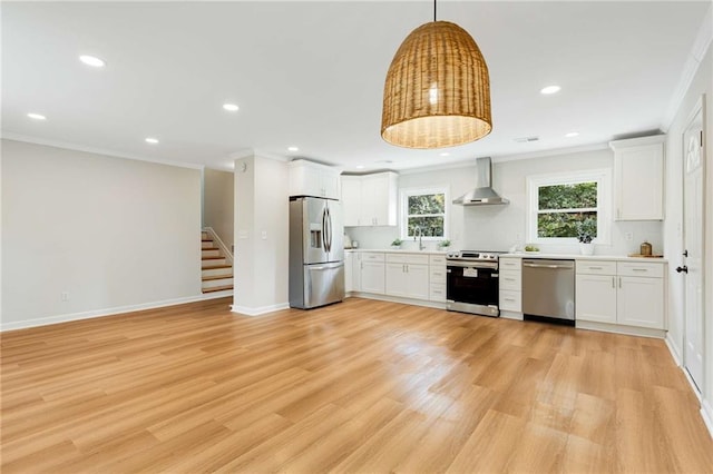 kitchen featuring ornamental molding, stainless steel appliances, wall chimney range hood, decorative light fixtures, and white cabinetry