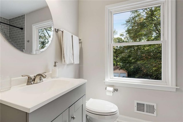 bathroom with tiled shower, a wealth of natural light, vanity, and toilet