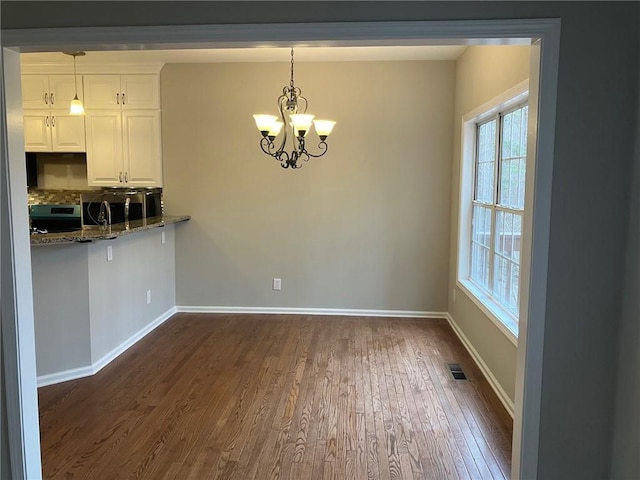 unfurnished dining area featuring plenty of natural light, a notable chandelier, and dark hardwood / wood-style flooring