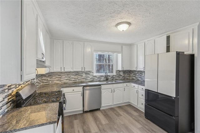 kitchen featuring sink, white cabinetry, dark stone countertops, stainless steel appliances, and light hardwood / wood-style floors