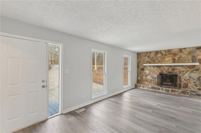 unfurnished living room featuring wood-type flooring, a stone fireplace, and a textured ceiling