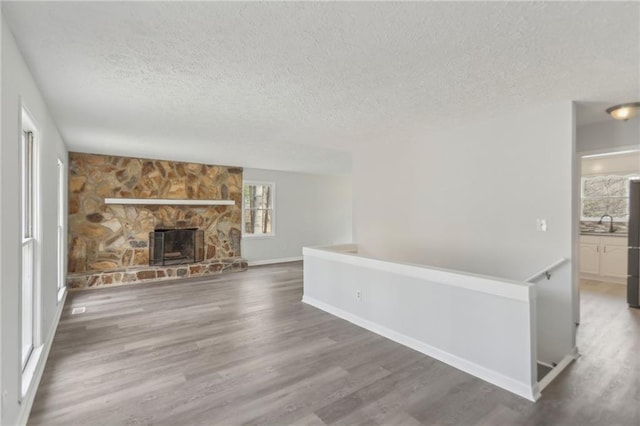 unfurnished living room featuring dark hardwood / wood-style flooring, a stone fireplace, and a textured ceiling