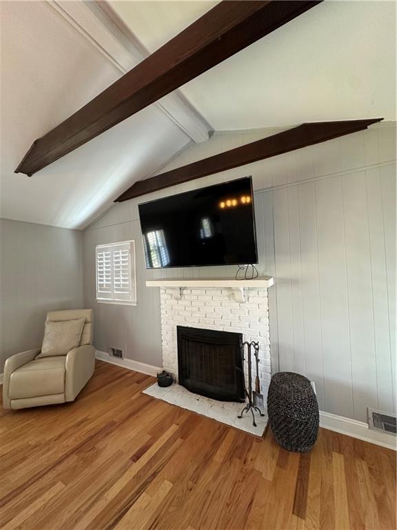 living area with visible vents, vaulted ceiling with beams, wood finished floors, and a fireplace