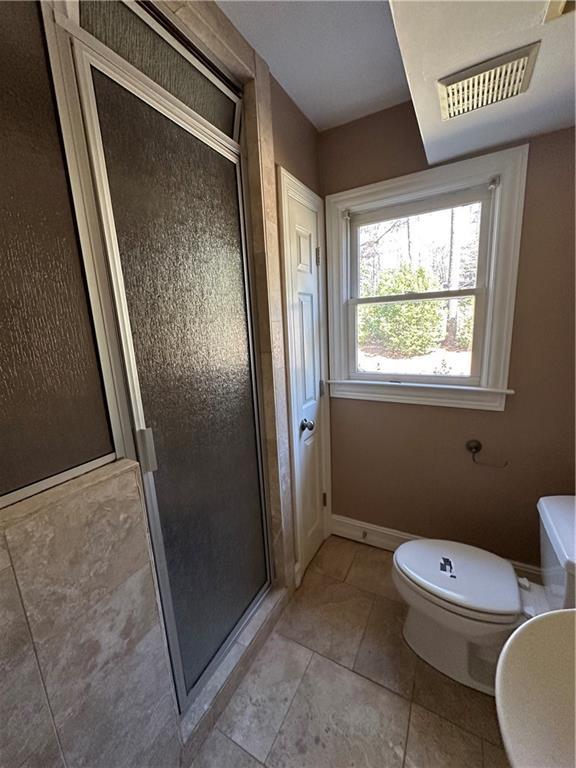 bathroom featuring tile patterned flooring, visible vents, baseboards, toilet, and a stall shower